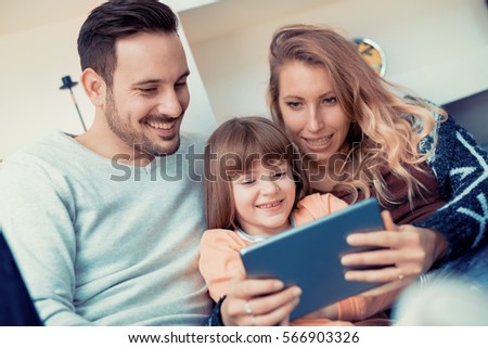 Happy family- mother, father and daughter at home,watching cartoons on a tablet.