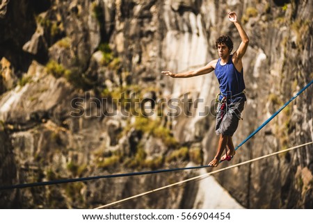 Athlete walking in slackline / highline / tight rope in a rock mountain Royalty-Free Stock Photo #566904454