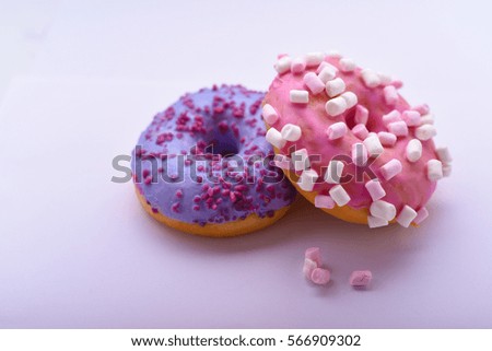 Purple donut with chocolate sprinkles and pink donut with marshmallows on a light background with colored sprinkles