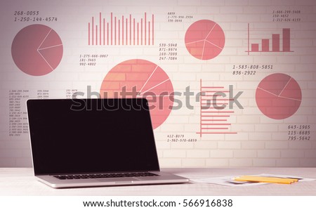 A professional laptop with blank screen sitting on a white office desk in front of wall full of pie charts and graphs concept