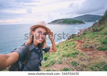 Traveling and technology. Young woman with hat and backpack taking selfie near the sea.