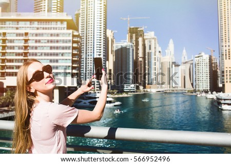 Woman in sunglasses looks over her shoulder before taking picture of skyscrapers on her iPhone