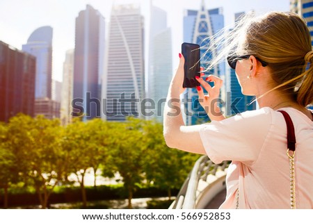 Look from behind at blonde lady taking picture on her iPhone standing somewhere in the city