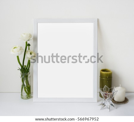 White poster mockup with tender flowers ranunculus in vase and candles on a light wall background. Template frame mock up for your content.