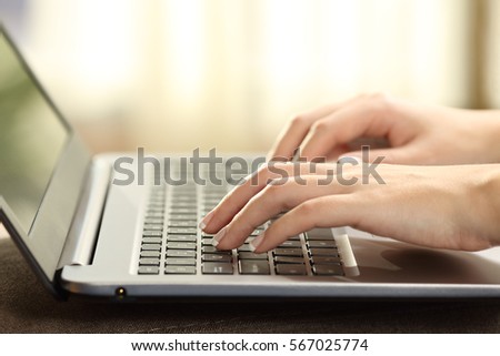 Close up of a woman hands typing on a laptop keyboard with a window and a warm light in the background