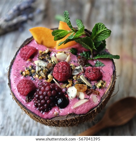 mixed berries smoothie in almond milk with dates, grounded grilled black sesame, chia seed and banana. Topped with berries, persimmon, almond, black sesame, granola. Serve in coconut bowl.  Royalty-Free Stock Photo #567041395