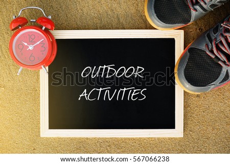 Fitness and Healthcare Concept. Top view of alarm clock, sport shoe and chalkboard written with OUTDOOR ACTIVITIES on sand background.