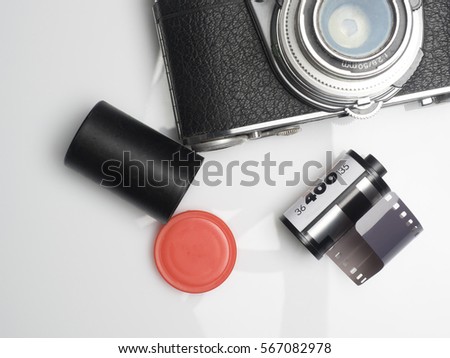 Roll of 35mm unexposed film on white background with camera and cannister