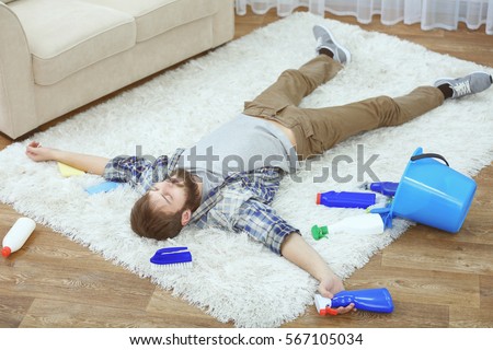 Funny young man tired of cleaning carpet at home Royalty-Free Stock Photo #567105034
