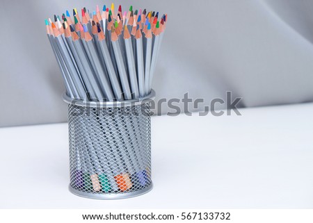 Color pencils in busket on wooden white table with gray background