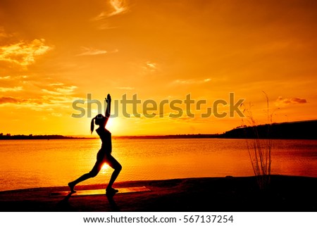 Silhouette of beautiful woman practicing yoga above the dam at the sky sunset.
