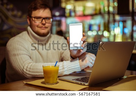 Young man in glasses showing smartphone in cafe