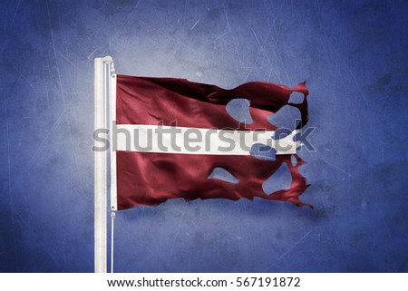 Torn flag of Latvia flying against grunge background.