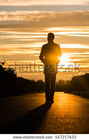 Silhouette of a man walking on a road at sunset. 