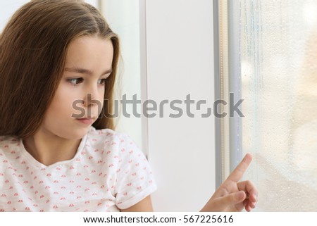 Sad little girl drawing on window glass at home