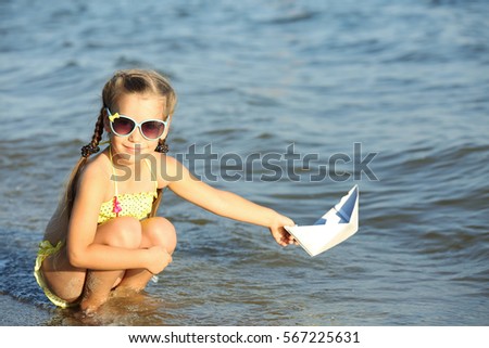Cute girl playing with paper ship in sea