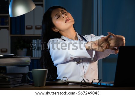 Photo of a tired young female doctor stretch in her medical office at late night. pretty mixed race asian chinese woman model. medical and health concept