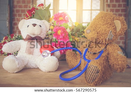 Two teddy bears sitting on the wood table, with the stethoscope and heart ball. Heart care concept