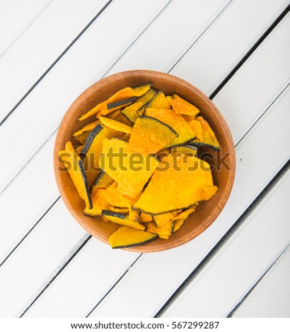 Pumpkin chips in wooden bowl over white background