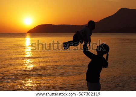 Mother and daughter at sunset, mom throws up the child, the sea, mountains in the background
