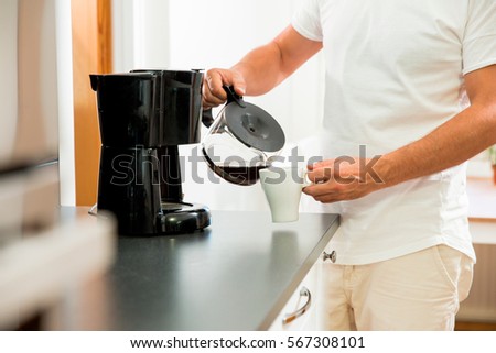 Man in the kitchen pouring a mug of hot filtered coffee from a glass pot. Having breakfast in the morning Royalty-Free Stock Photo #567308101