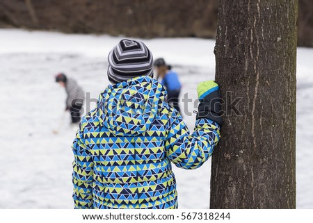 Child watching other children playing ice hockey on a frozen lake or river