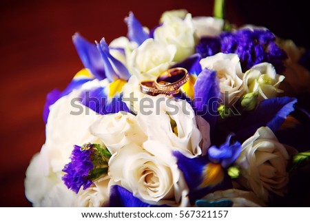 Two wedding rings with white and blue flower in the background.