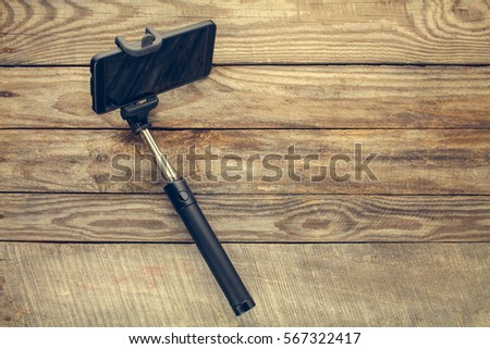 Mobile phone on selfie stick on old wooden background. Toned image.  