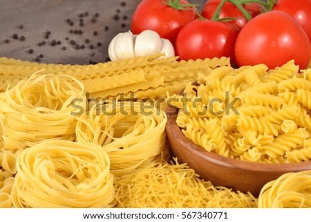 Uncooked Italian pasta, ripe tomatoes branch, garlic and black pepper on a wooden background