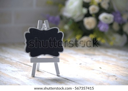 A small vintage blackboard on wooden table and blur bouquet background. ideal for romantic theme . Text space