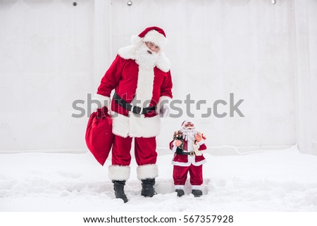 Santa Claus standing with Little Santa Claus toy and holding red sack 
