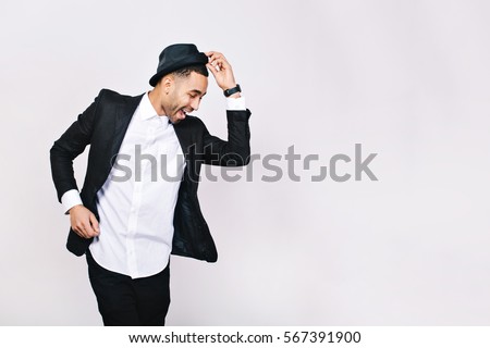 Attractive young man in suit dancing, having fun on white background. Stylish outlook, hat, successful businessman, happy, expressing true positive emotions, funny. Place for text