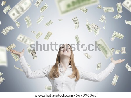 Portrait of a happy blond woman wearing a white blouse standing near a gray wall. Dollars are falling at her from the sky.