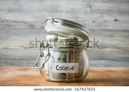 Dollar bills in glass jar isolated on wooden background. Saving money concept for college. 
