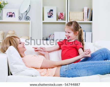 Young  mother lying on the sofa and playing with her happy loving  little daughter - indoors