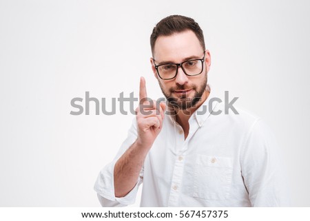 Image of concentrated young bearded man dressed in white shirt wearing glasses gesturing with hand and pointing isolated over white background.
