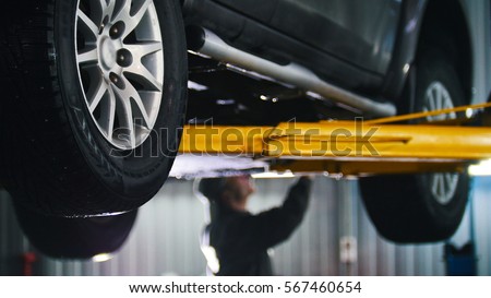 Car lifted in automobile service for fixing, worker repairs detail, telephoto Royalty-Free Stock Photo #567460654