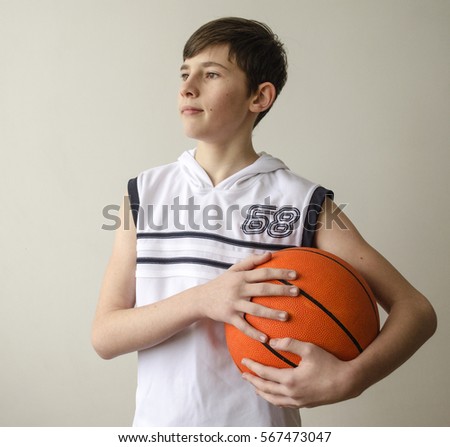 Teenager boy in a white shirt with a ball for basketball on a light background

