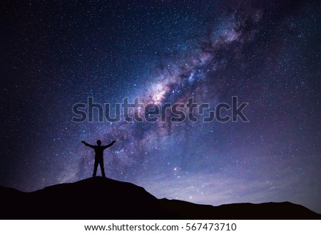 Milky Way landscape. Silhouette of Happy man standing on top of mountain with night sky and bright star on background.  Royalty-Free Stock Photo #567473710