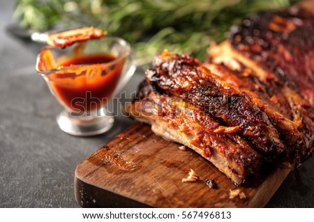 Delicious barbecued ribs seasoned with a spicy basting sauce and served with chopped fresh vegetables on an old rustic wooden chopping board in a country kitchen Royalty-Free Stock Photo #567496813