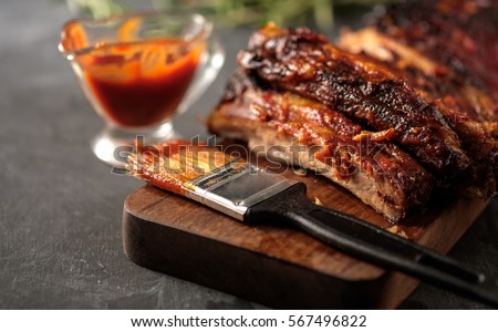 Delicious barbecued ribs seasoned with a spicy basting sauce and served with chopped fresh vegetables on an old rustic wooden chopping board in a country kitchen Royalty-Free Stock Photo #567496822