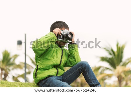Little Asian kid shoots photographs with film camera in the Park.