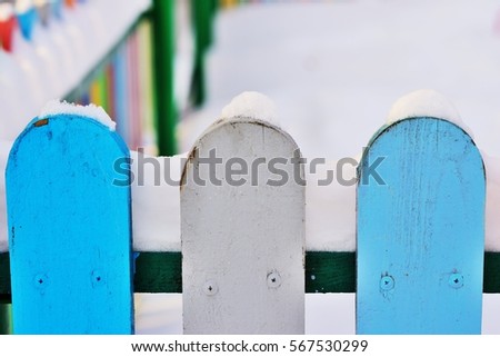 Part of ?olorful vertical wooden fence painted in red, blue, green, orange, yellow and gray colors under snonw