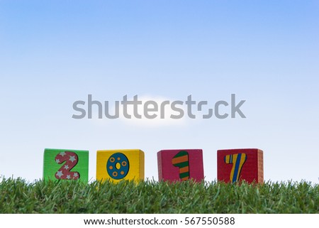 Wood block squre shape paint number in each a piece is 2017 for use for use meaning is happy new year on green grass and a blue sky background