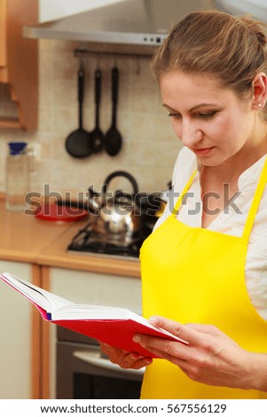 Housewife woman reading cookbook in kitchen. Mature female in apron at home.
