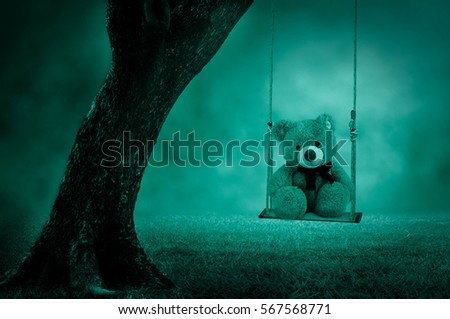Teddy bear sitting under a tree swing cute.