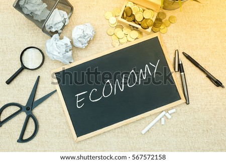 Business Concept : ECONOMY word on black board with office table background.