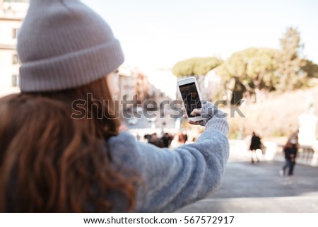 Back view of woman taking pictures with blank screen mobile phone in the city