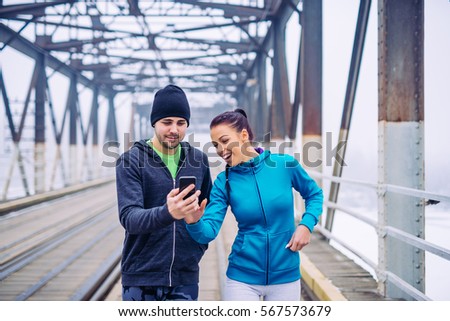 Portrait of an athletic couple having fun with mobile phone on the train bridge in the break.