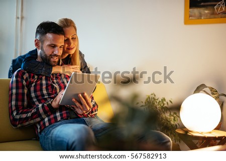 Close up portrait of an attractive married couple using digital tablet. Wife is hugging her husband from behind. They are both feeling happy and in love.